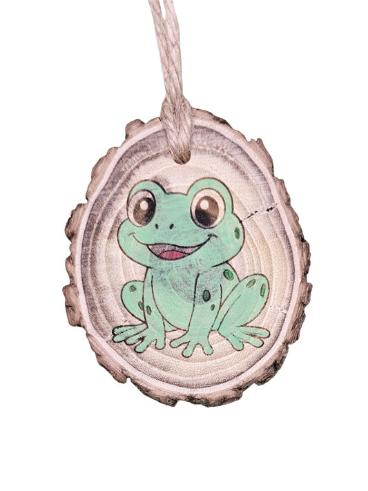 A wood burned Christmas tree ornament depicting a frog with a laser engraved hand drawn design, suspended by a twine string.