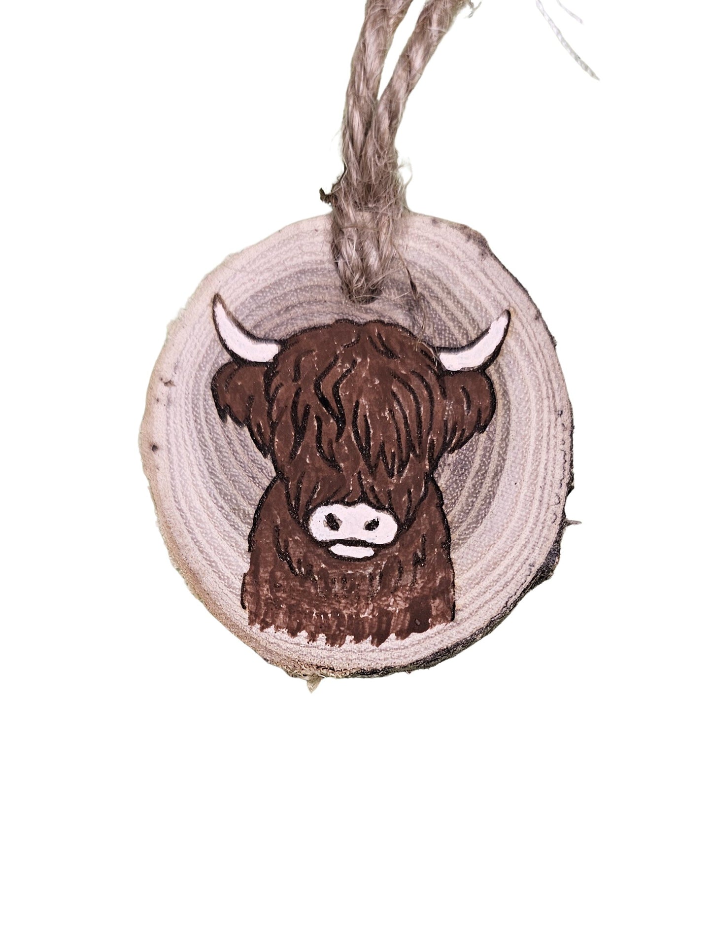 A wood burned Christmas tree ornament depicting a highland cow with a laser engraved hand drawn design, suspended by a twine string.