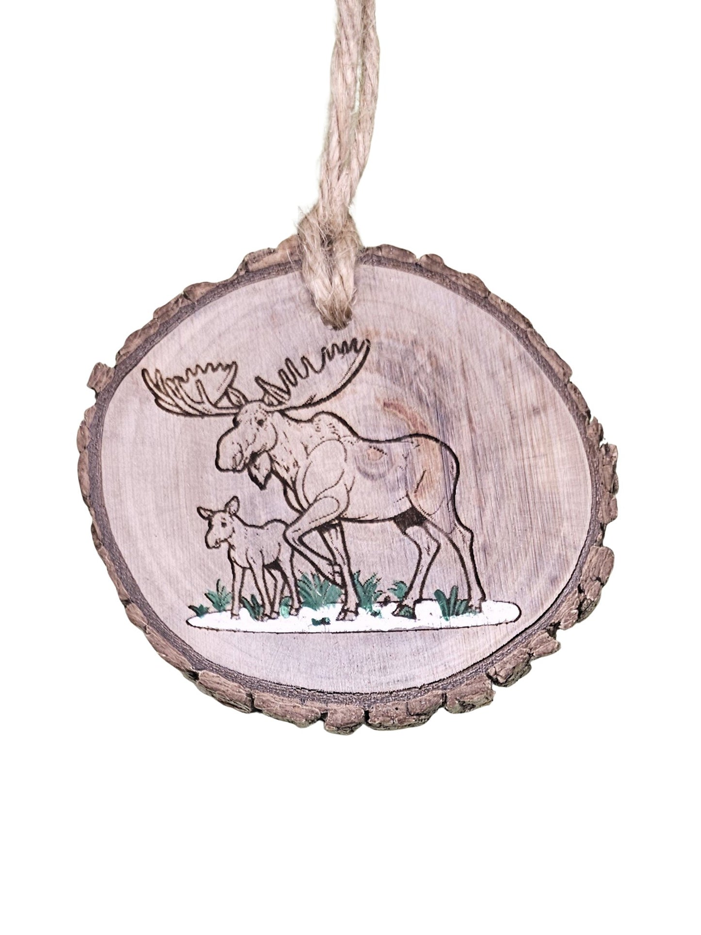 A wood burned Christmas tree ornament depicting an adult and baby moose with a laser engraved hand drawn design, suspended by a twine string.