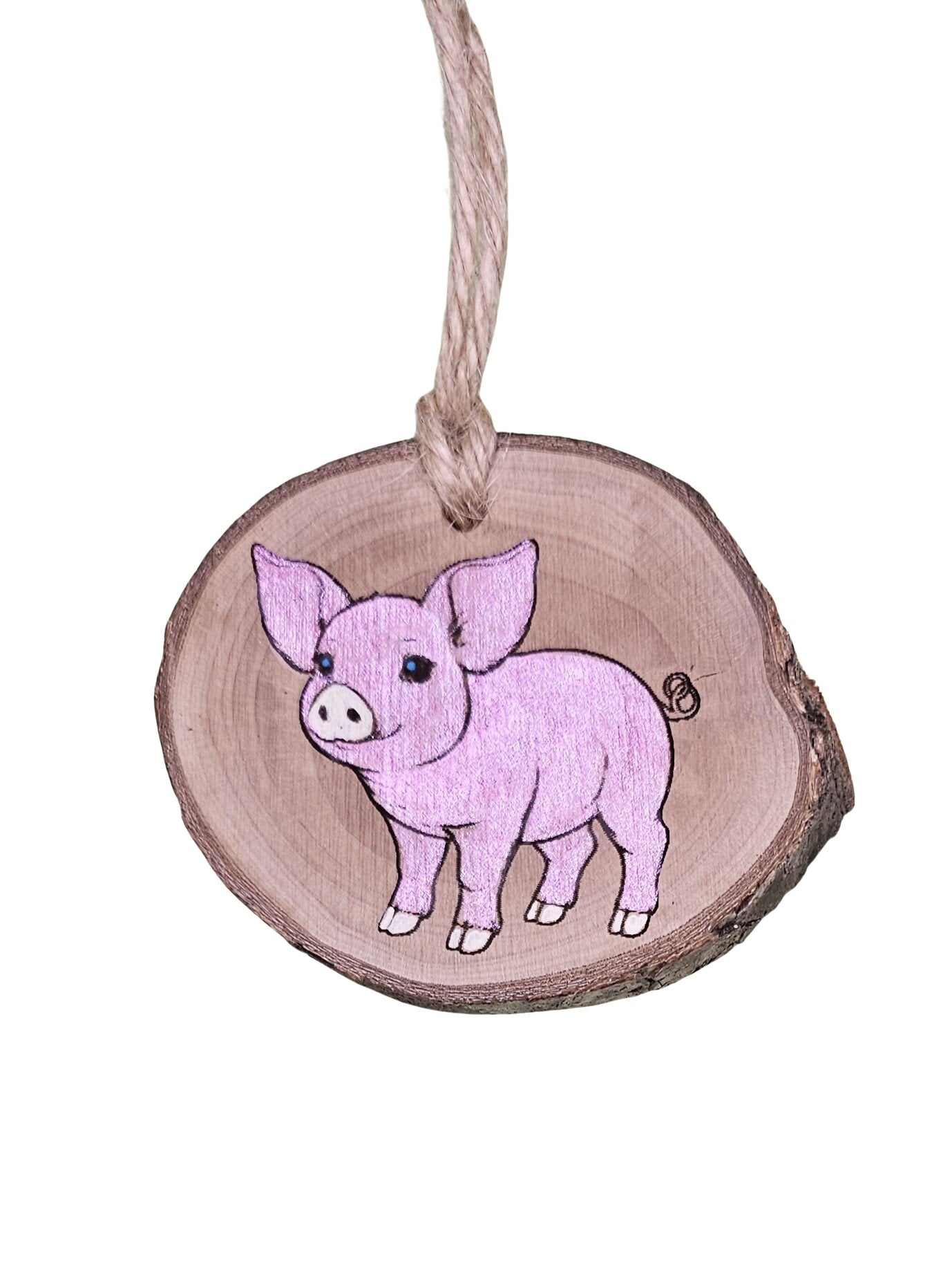 A wood burned Christmas tree ornament depicting a pink pig with a laser engraved hand drawn design, suspended by a twine string.