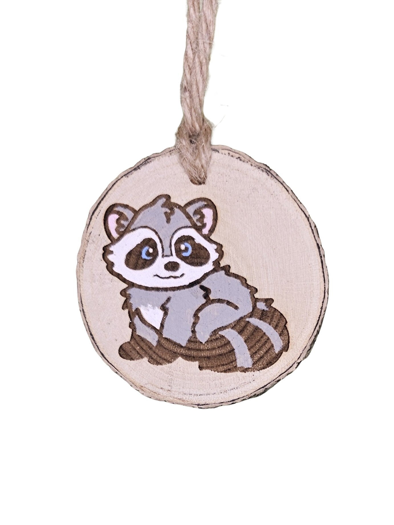 A wood burned Christmas tree ornament depicting a racoon with a laser engraved hand drawn design, suspended by a twine string.