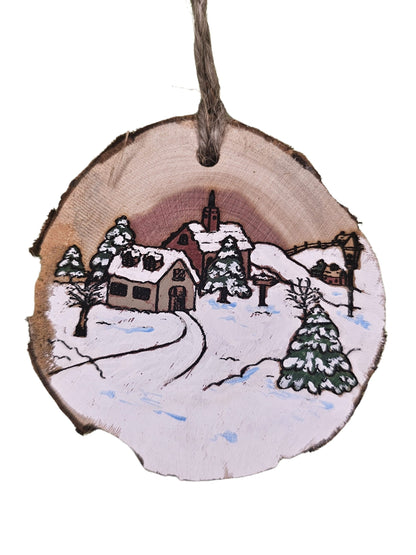 Wooden ornament with a winter scene of a house and trees painted on it.