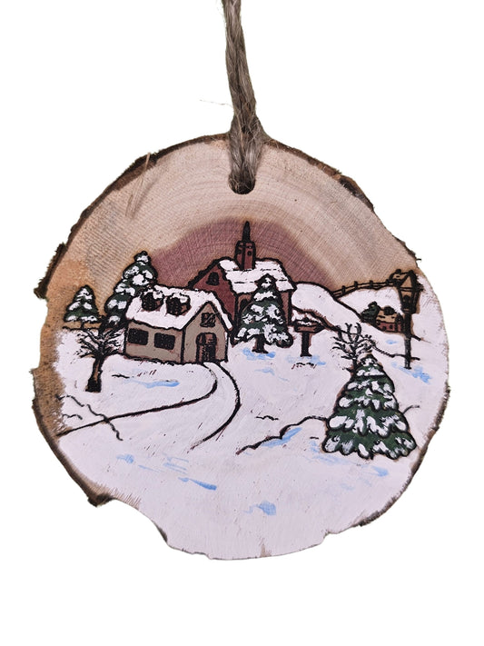 Wooden ornament with a winter scene of a house and trees painted on it.
