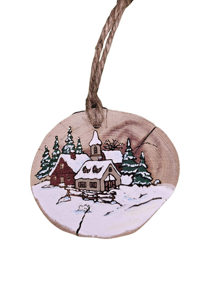 Wooden ornament with a winter scene of a village and trees, hanging on a string.